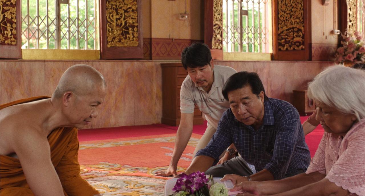 A Buddhist monk sits facing a family kneeling on a temple floor
