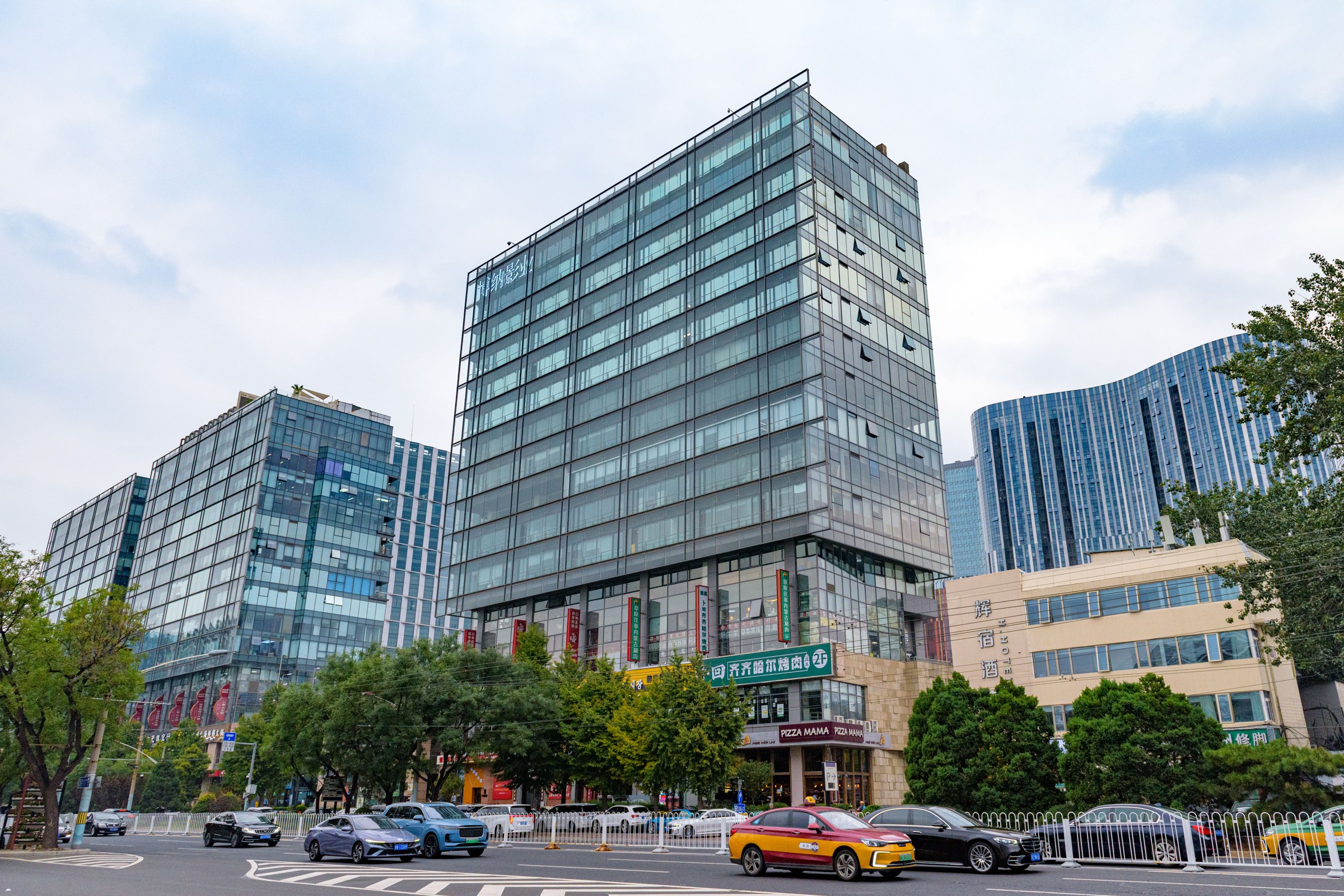 A glass office tower on a Beijing street corner with taxis and cars passing in front