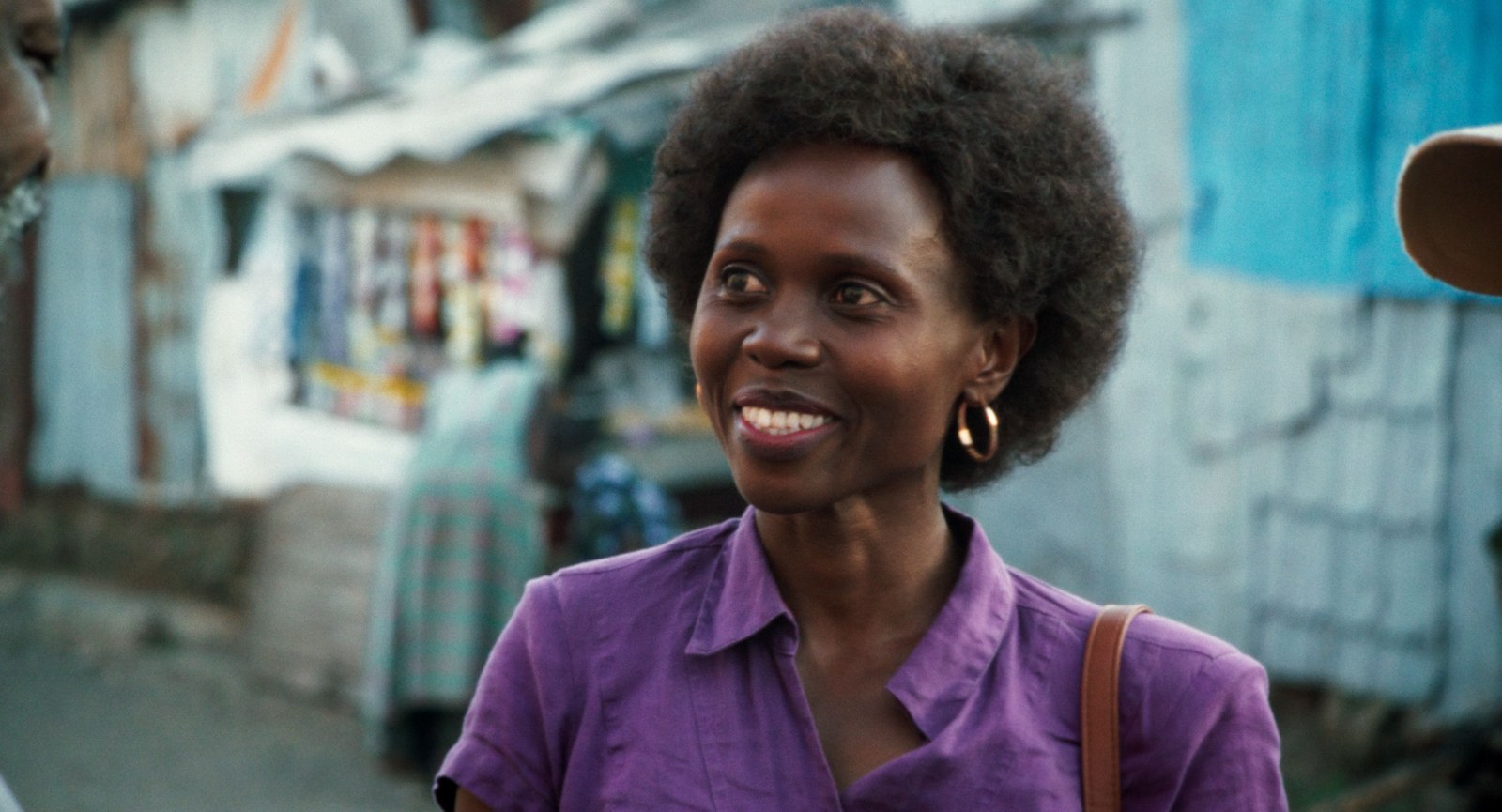 Eliane Umuhire, smiling, in a purple shirt on a Nairobi street lined with shacks, in a still from Call Me Queen