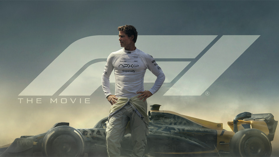 Brad Pitt in a white racing suit stands in front of a Formula One car beneath the F1 The Movie logo