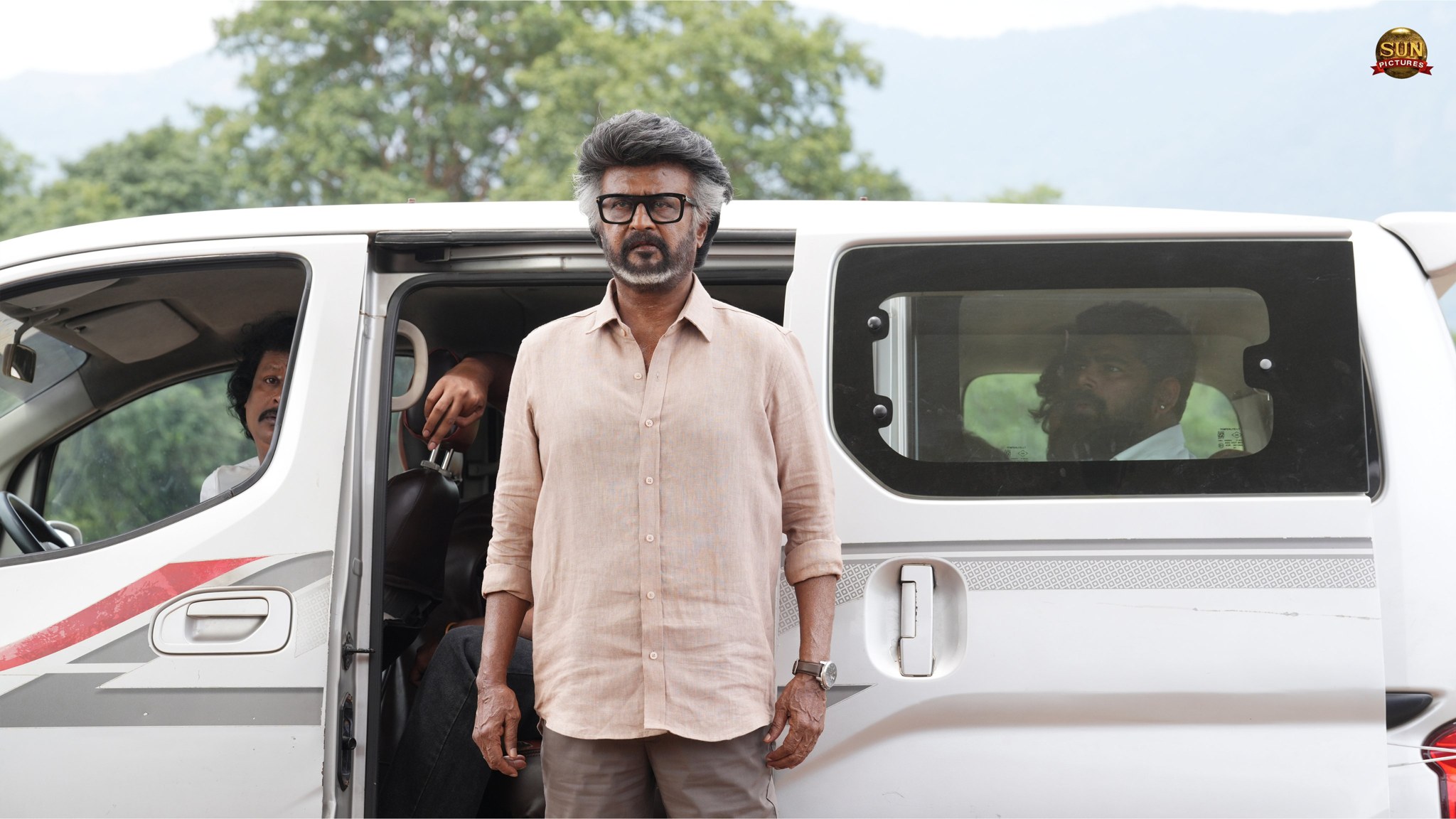 Rajinikanth in glasses and a linen shirt stands in front of a white van on a country road, in a still from Jailer 2