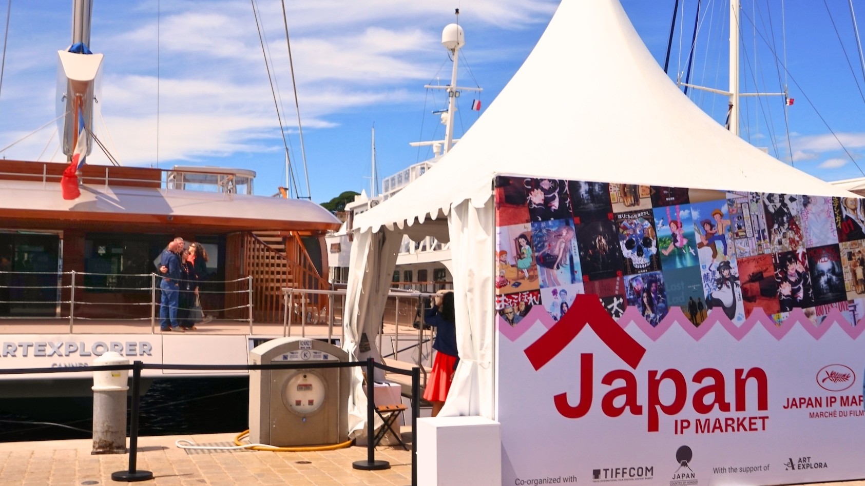 A white Japan IP Market marquee beside the Art Explora catamaran in Cannes harbour