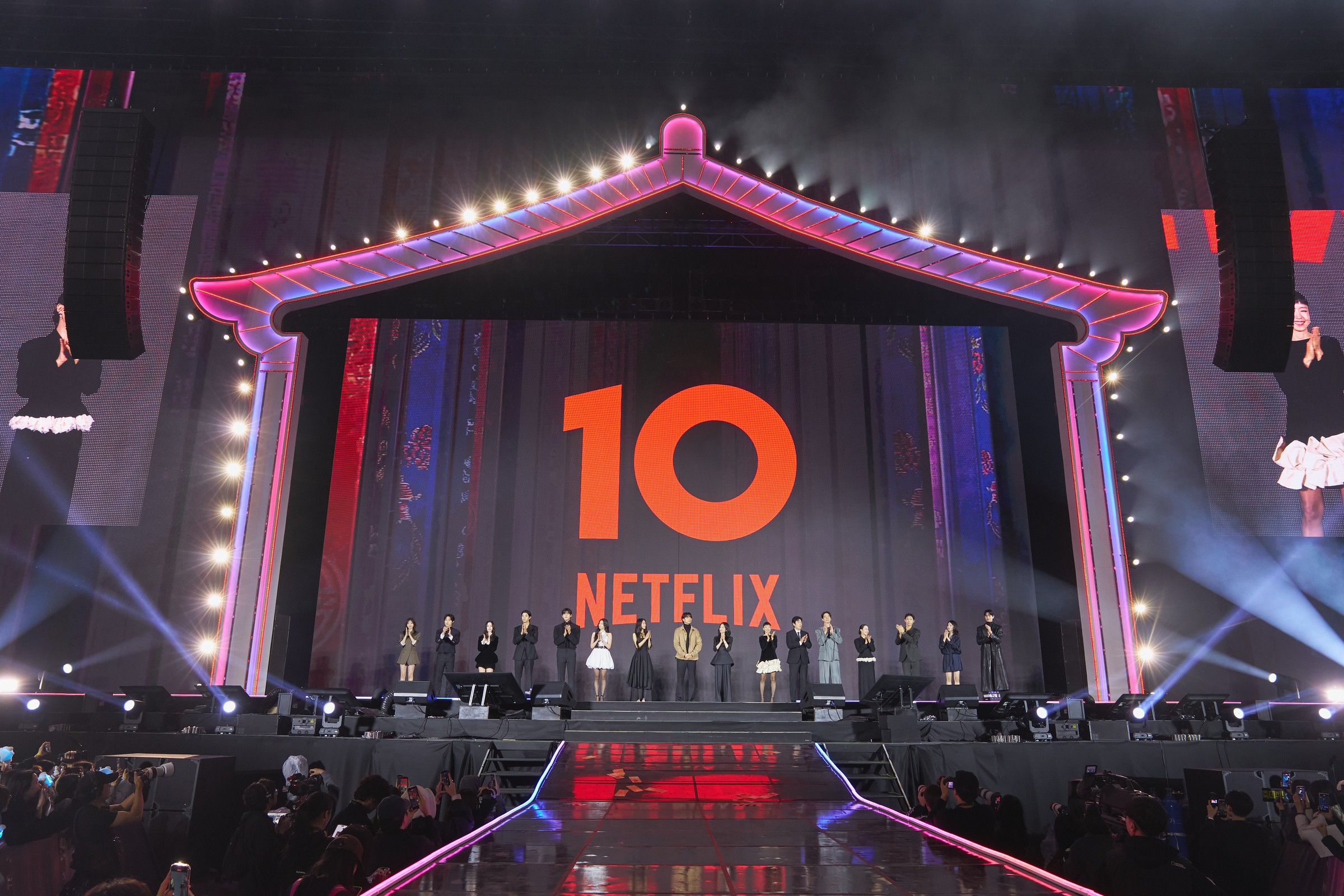A row of guests on a stage under a lit Korean-style roof frame, with a large red "10 Netflix" sign behind them