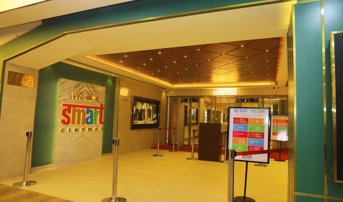 The entrance of a PVR INOX SMART Cinemas site with the brand logo on a marble wall, queue barriers and glass doors