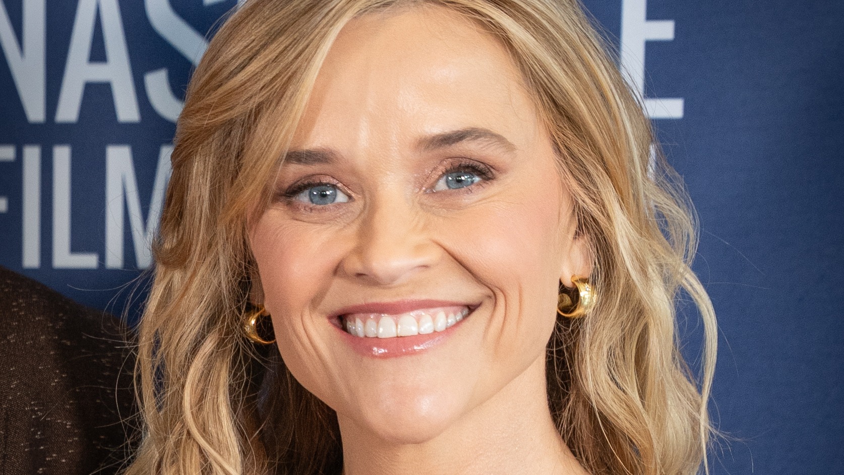 Reese Witherspoon, smiling, in front of a blue Nashville Film Festival backdrop