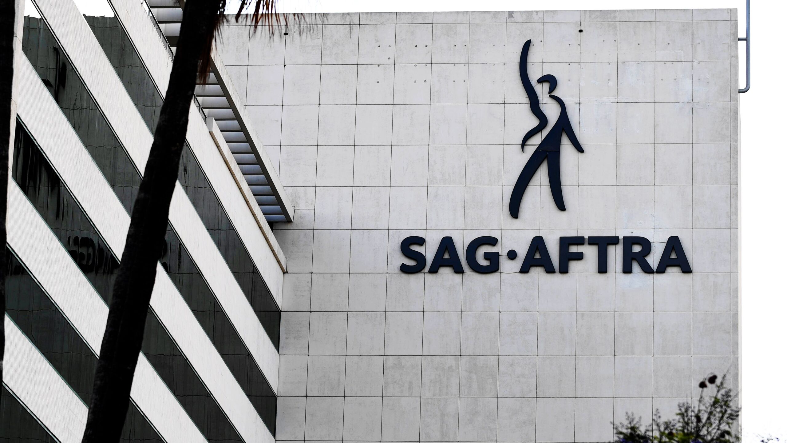 A pale tiled office facade bearing the SAG-AFTRA logo and name, beside a palm tree trunk and a parking structure