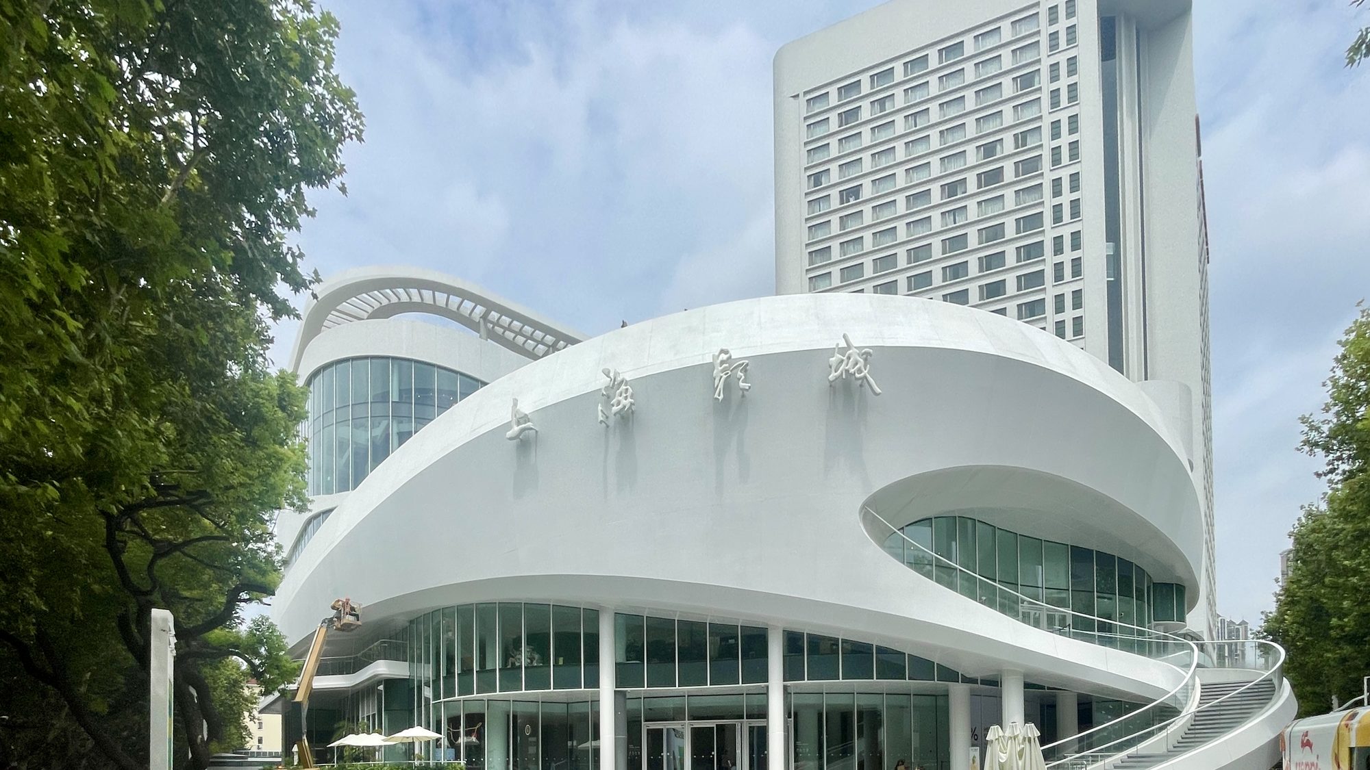 The curved white facade of the Shanghai Film Art Center, with the characters 上海影城 above a glass-fronted ground floor and a hotel tower behind