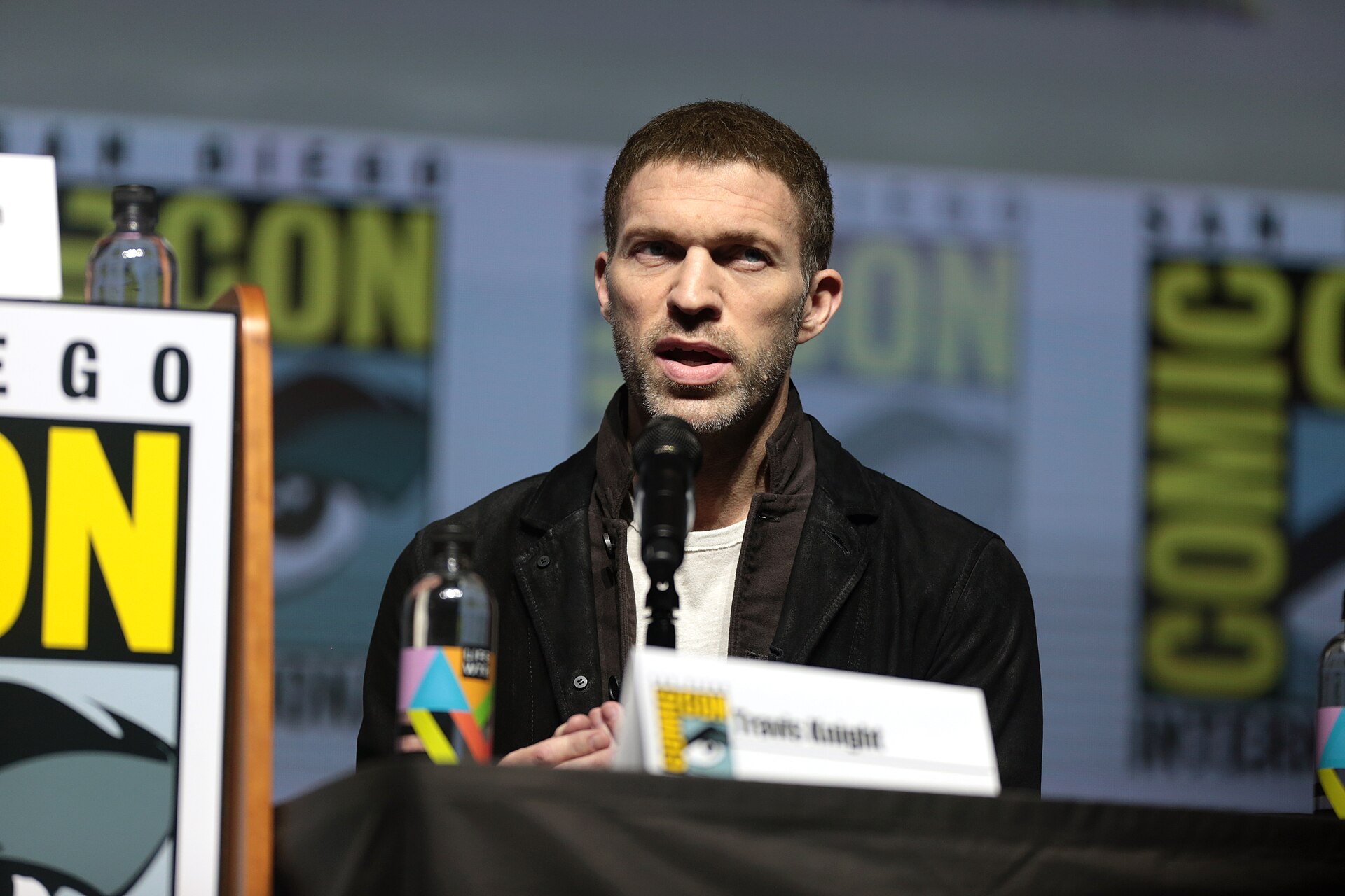 Travis Knight speaking into a microphone on a Comic-Con panel in 2018
