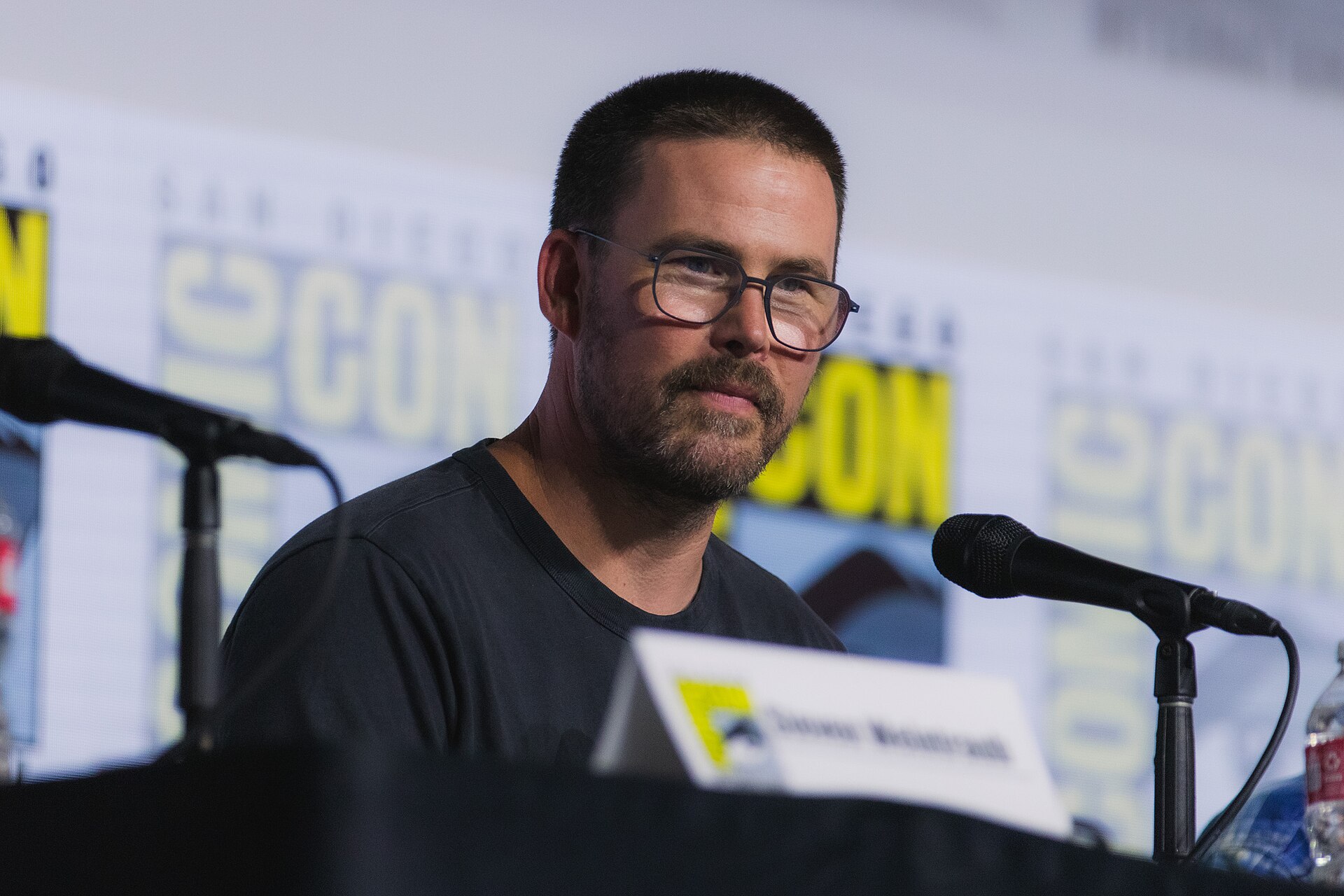 Zach Cregger in glasses seated at a microphone on a San Diego Comic-Con panel